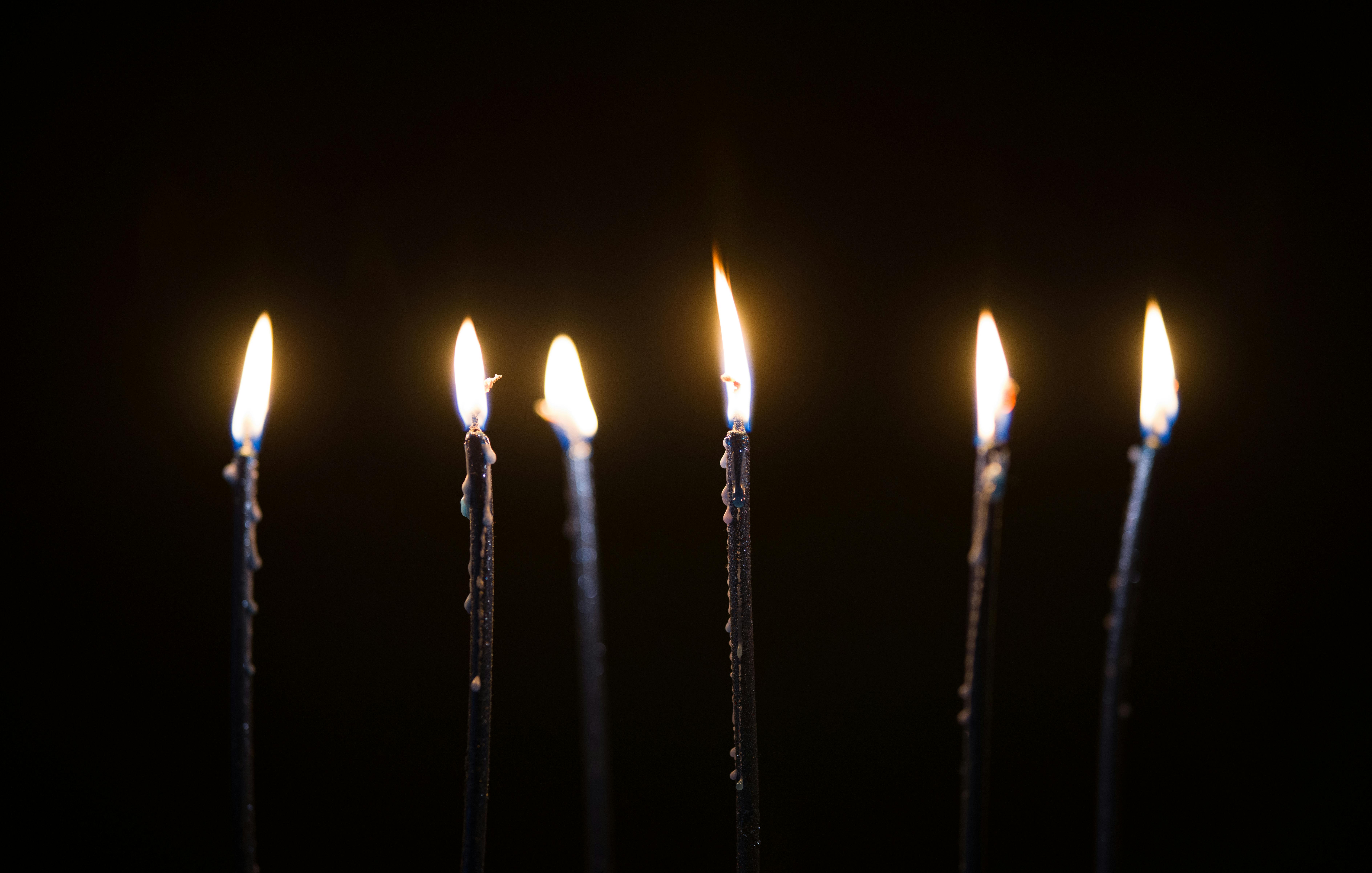 Six slender candles burning brightly against a black background in a peaceful setting.