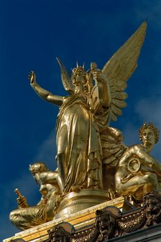 Majestic golden statues atop the Paris Opera House, glistening against a deep blue sky.