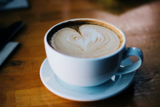 A warm cappuccino with heart-shaped latte art in a white mug on a wooden table.