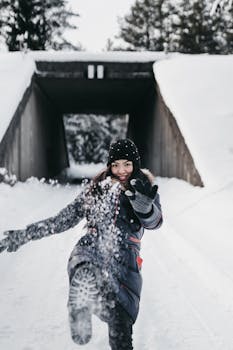 Cheerful woman in winter clothes kicking up snow, enjoying a cold day outdoors.