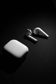 Black and white close-up of wireless earphones on a dark background.