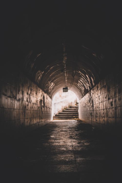 Free A dark, moody tunnel with a light source at the end leading to a staircase. Stock Photo