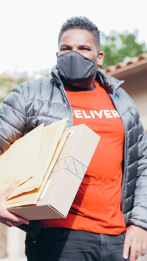 Free Delivery man in facemask holding packages, embracing new normal safety measures. Stock Photo