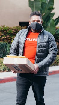A delivery man in a face mask holding packages outdoors, emphasizing safe practices.