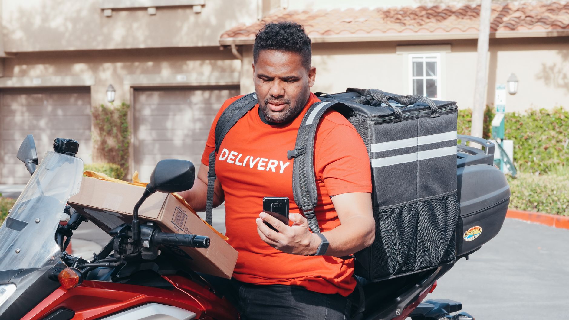 Courier on a motorcycle with a box and phone, showcasing efficient delivery service.