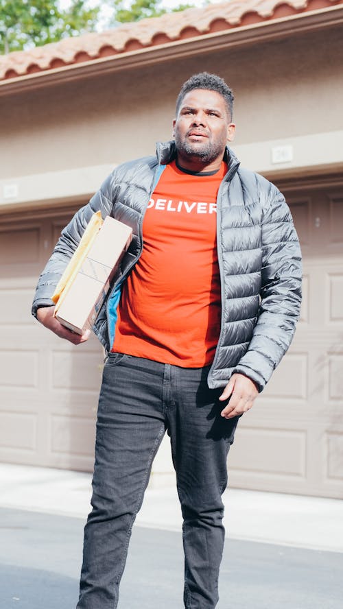 Man in Red Shirt and Gray Jacket Carrying a Package and Mail