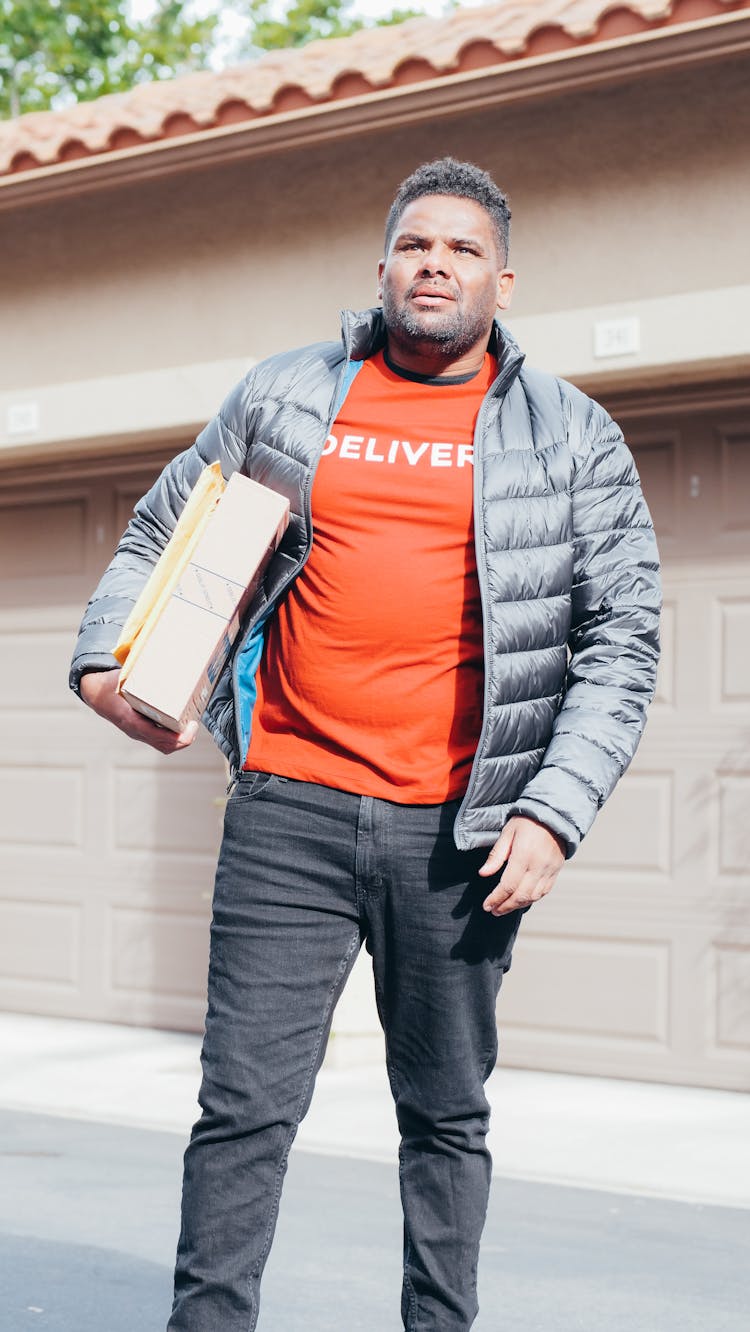 Man In Red Shirt And Gray Jacket Carrying A Package And Mail