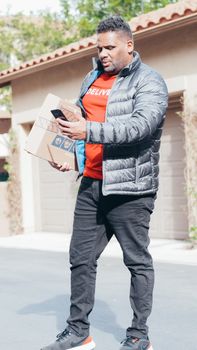 Courier in a jacket delivering packages while checking mobile outside a house.