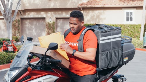 Free Man in Orange Shirt Riding on a Motorbike Making a Delivery Stock Photo