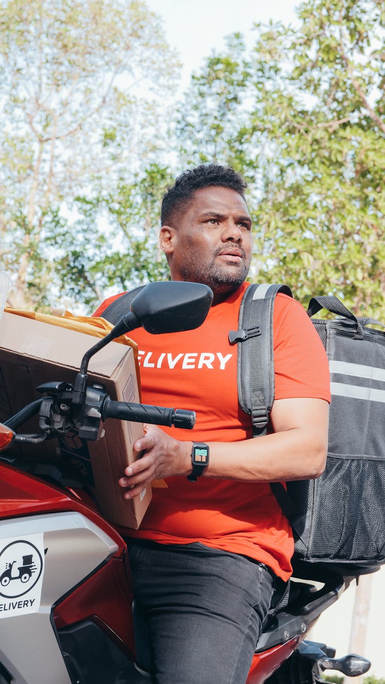 Man In Red T-shirt Riding On A Motorcycle With A Package And Mail For Delivery