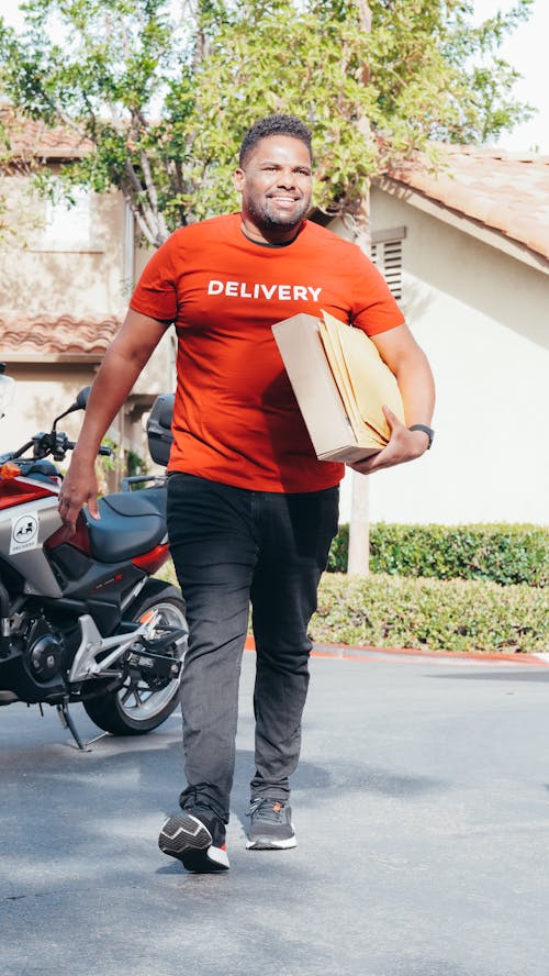 Smiling Man in Red Crew Neck T-shirt Carrying a Package For Delivery