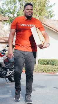 Smiling delivery person carries packages outdoors near a house with a motorcycle.