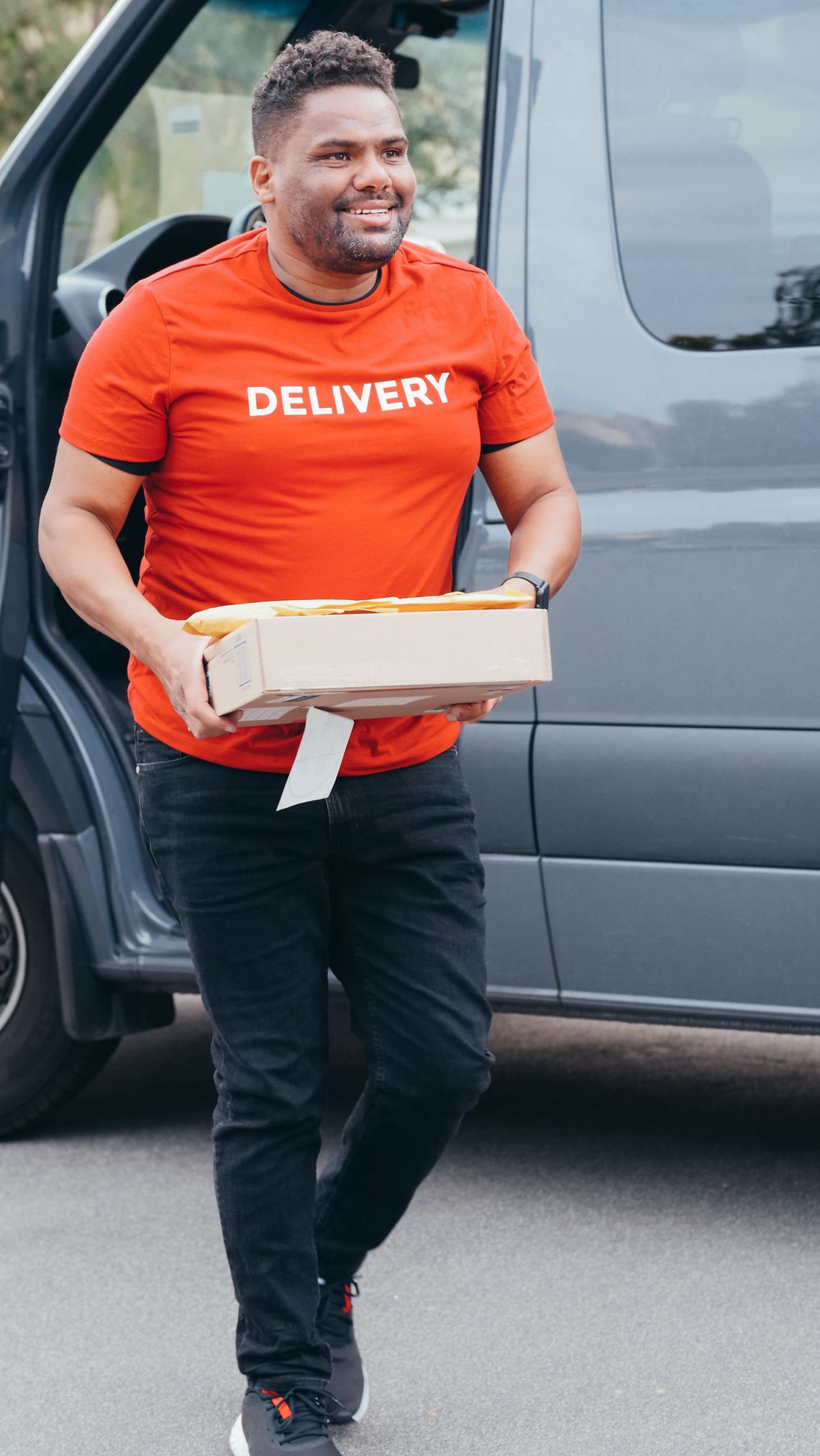 Smiling courier carrying a package beside a delivery van