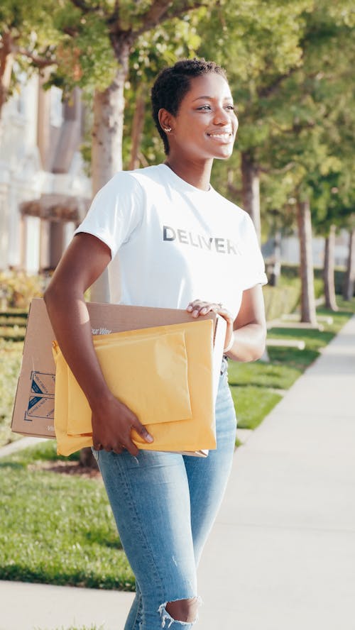 Woman in White Crew Neck T-shirt and Blue Denim Jeans Holding Brown Leather Handbag