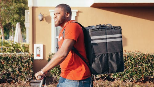 Man in Orange Crew Neck Shirt with Black Food Delivery Bag