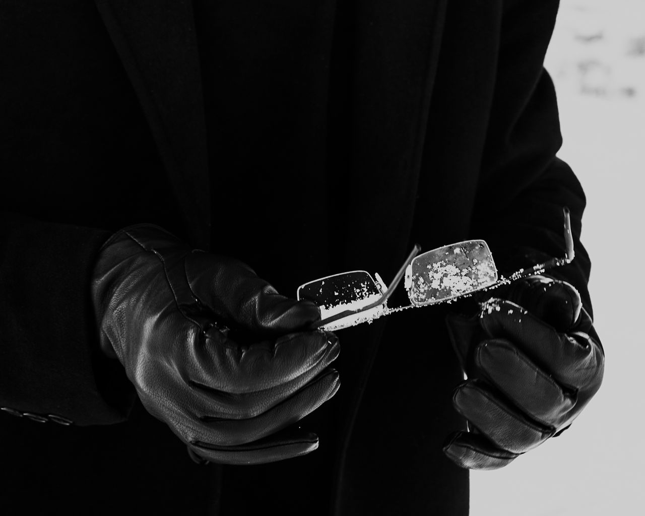 black gloved hands holding eyeglasses covered with snowflakes in a sty