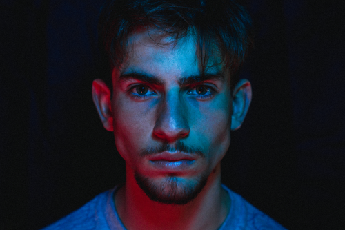 Free Close-up portrait of a man with dramatic blue and red lighting, capturing intense expression. Stock Photo