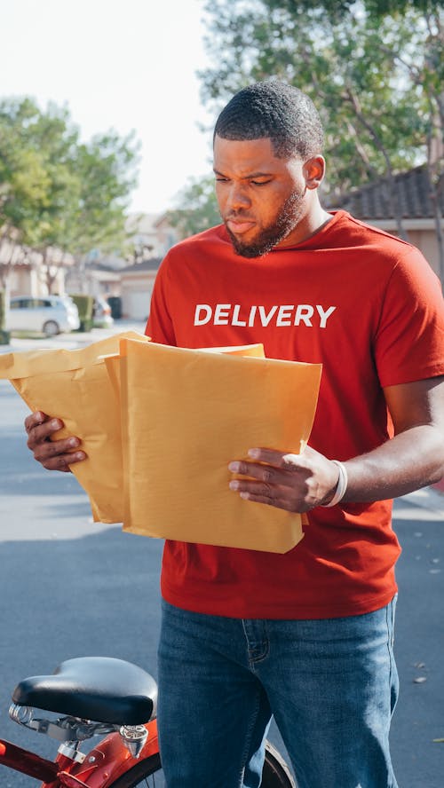 Man in Red Crew Neck T-shirt Holding Brown Parcels 