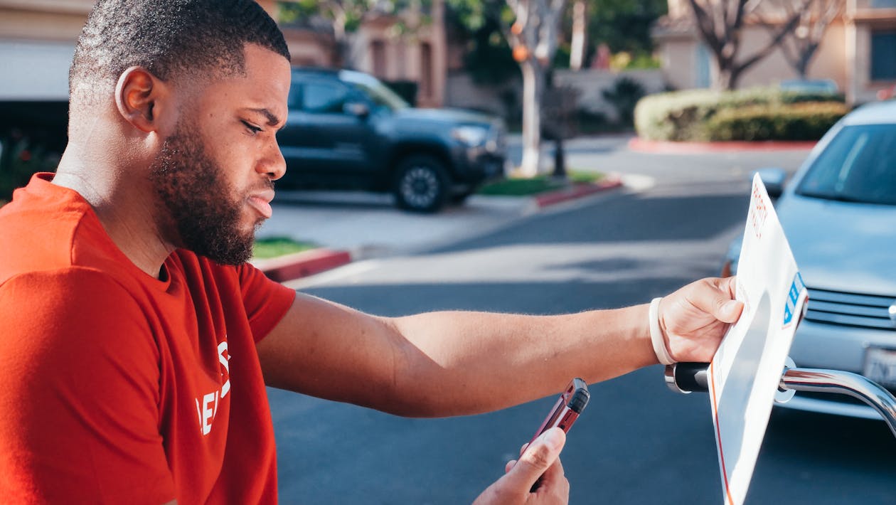 Man Holding a Parcel and Looking at His Cellphone