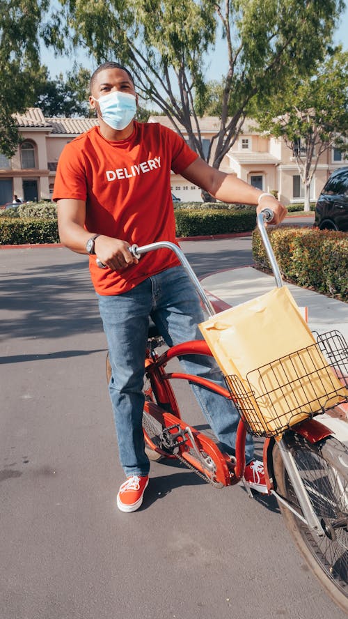 Deliveryman in Red Crew Neck T-shirt and Blue Denim Jeans Riding on Red Bicycle