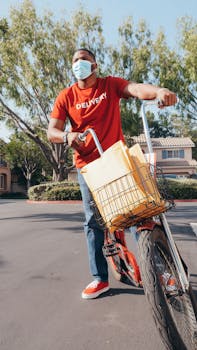 A delivery man wearing a mask riding a bicycle with packages in a residential area.