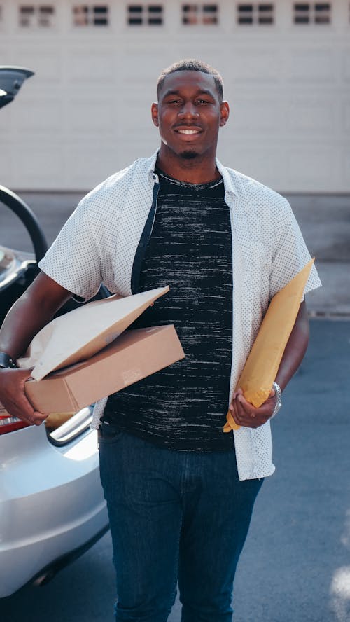 Man in White Button Up Shirt and Blue Denim Jeans Holding Packages