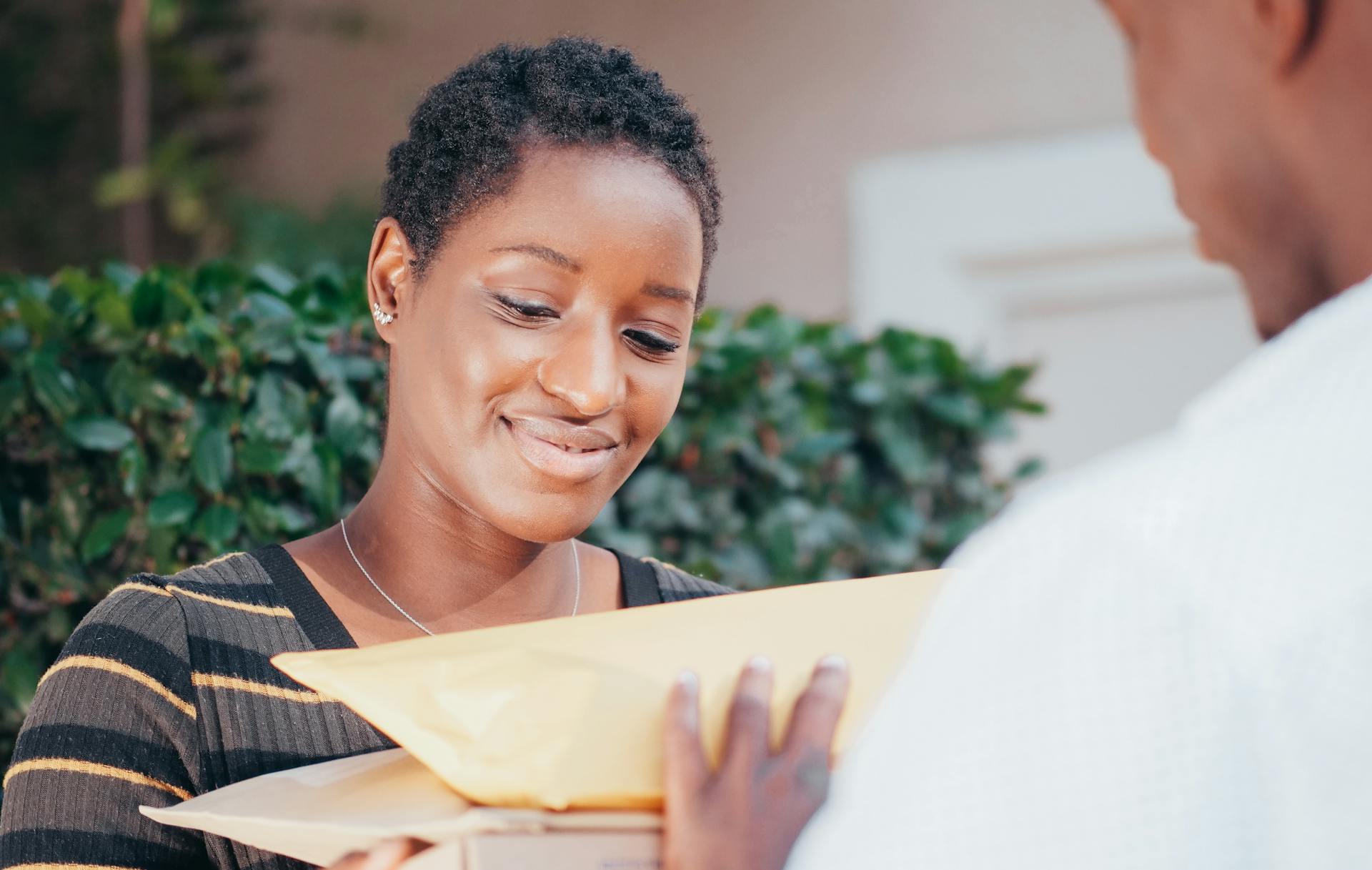 Smiling woman receiving a package from a courier in an outdoor setting.