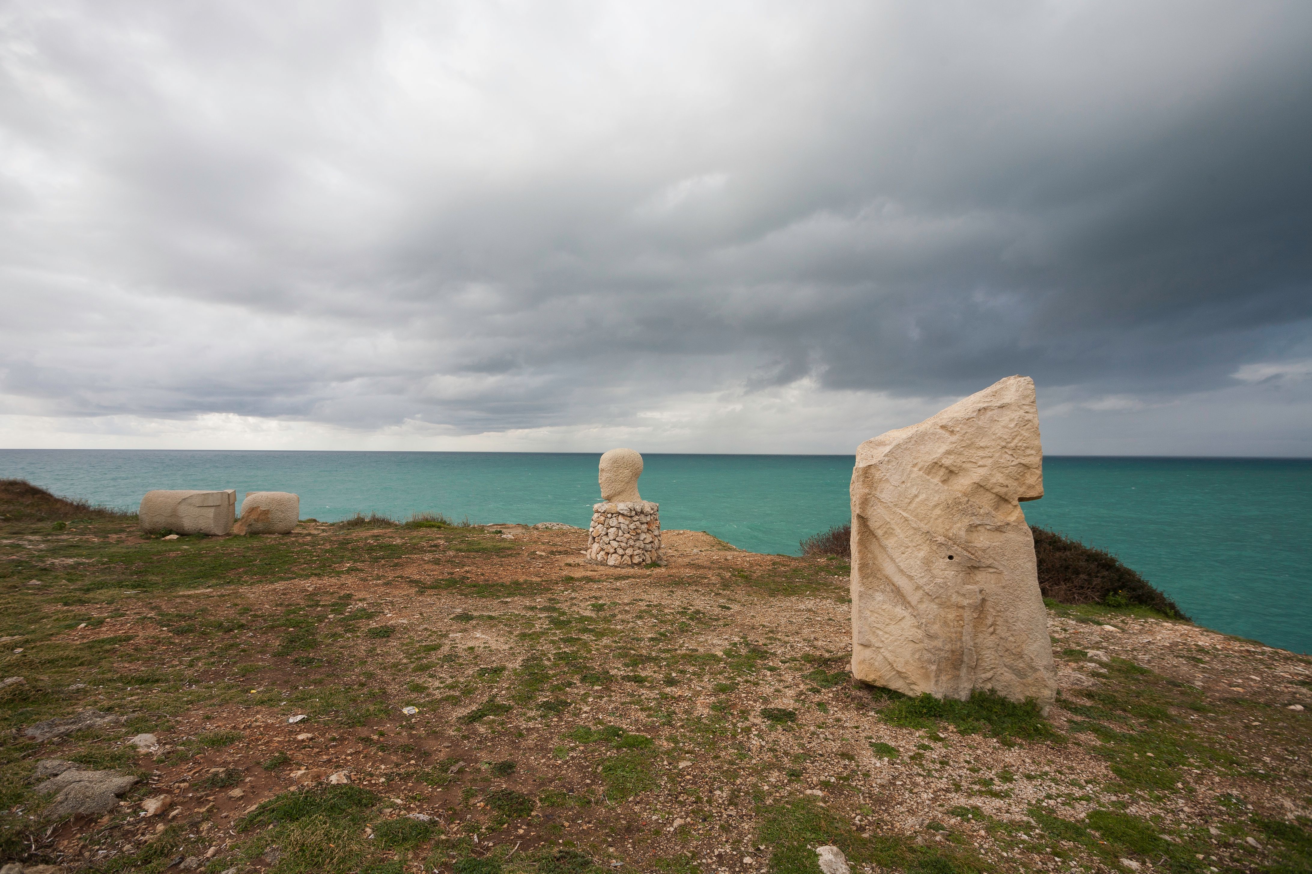Stone sculptures on a cliff overlooking the sea in Santa Maria di Leuca, Puglia, evoke timeless artistry and nature's serenity.