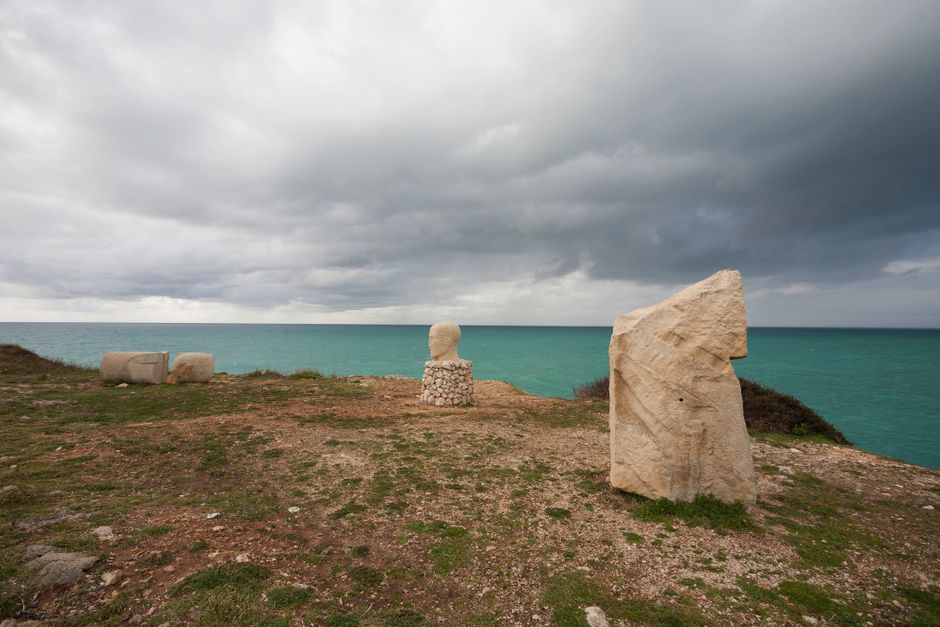 Stone sculptures on a cliff overlooking the sea in Santa Maria di Leuca, Puglia, evoke timeless artistry and nature's serenity.