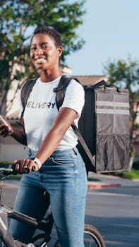 Smiling courier on a bicycle delivering a package outdoors in a sunny setting.
