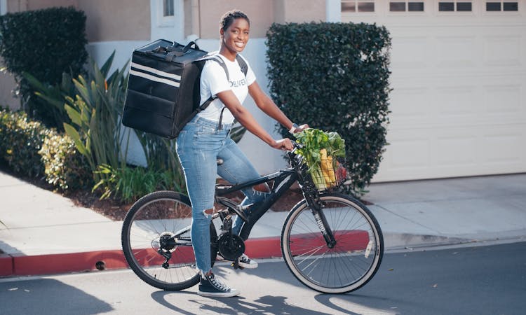 A Woman With Insulated Food Delivery Backpack Sitting On A Bike
