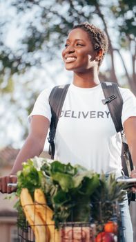 Smiling delivery woman biking with fresh fruits and vegetables outdoors on a sunny day.