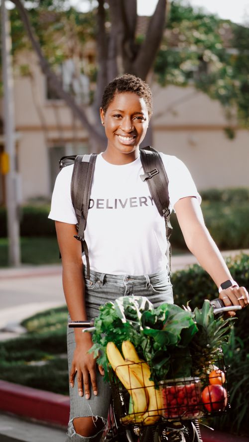 Free Woman delivering fresh fruits and vegetables by bicycle in a suburban neighborhood. Stock Photo