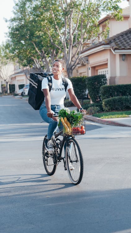 Uma Entregadora Carregando Bolsa Térmica Andando De Bicicleta Enquanto Passeia Na Rua