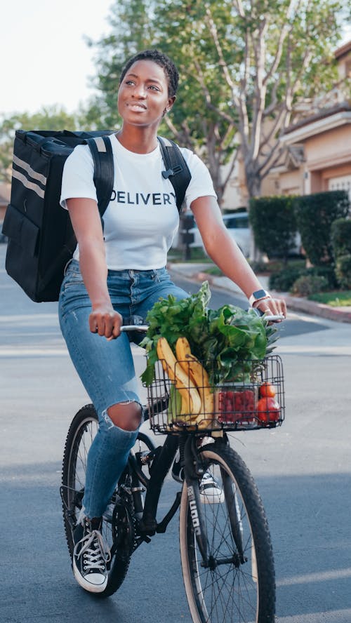 Woman in White Crew Neck T-shirt Carrying Green Vegetables and Fruits on Bicycle