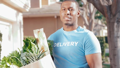 Man in Blue Crew Neck T-shirt Carrying Vegetables on Paper Bag