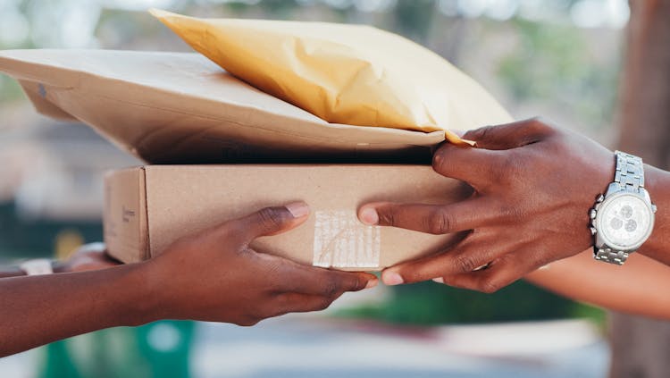 A Person Handing Out A Brown Box And Envelopes To A Person