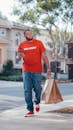 Man in Red Crew Neck T-shirt and Blue Denim Jeans Holding Brown Paper Bags