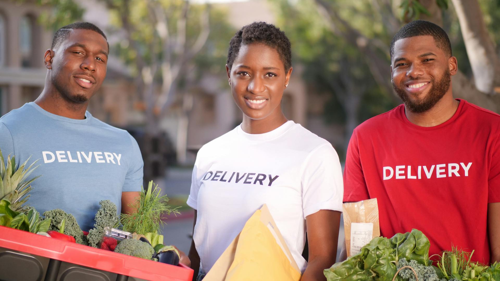 Smiling delivery team carrying fresh groceries and packages outdoors.