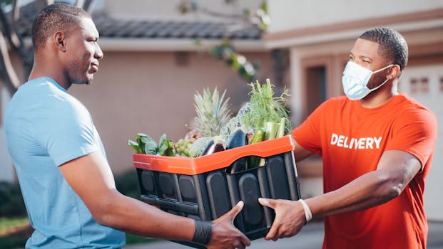 Two men exchanging a crate of fresh vegetables during a contactless delivery outdoors with safety measures.