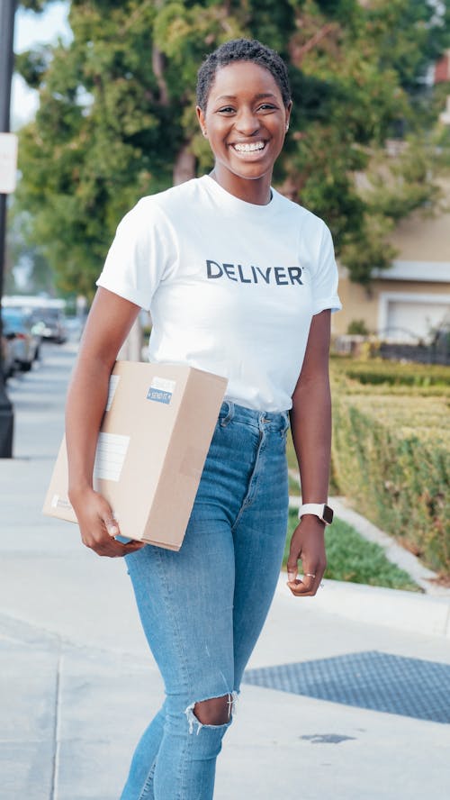 Woman in White Crew Neck T-shirt and Blue Denim Jeans Holding White Box