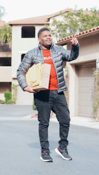 Smiling man making deliveries in a neighborhood, carrying packages and wearing casual clothing.