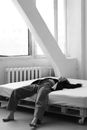 Black and white female in loose trousers and unbuttoned shirt lying on back on cozy bed in light room