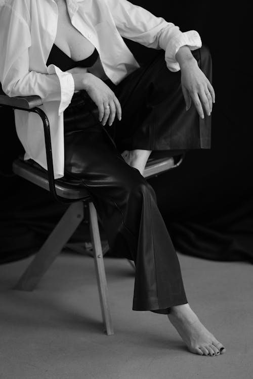 Grayscale Photo of Woman in White Dress Shirt and Black Pants Sitting on Chair