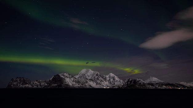 Scenic view of the Northern Lights over snowy mountains in Nordland, Norway.