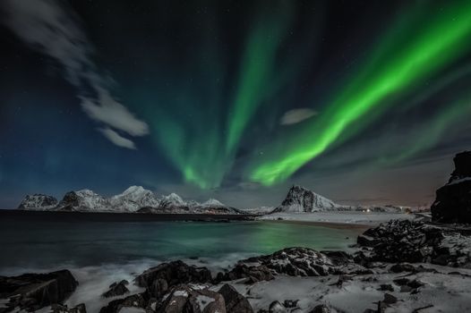 Majestic aurora borealis over snow-covered mountains at night in Nordland, Norway.