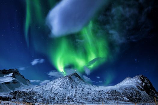 Breathtaking aurora borealis lights up the sky over snowy peaks in Norway.
