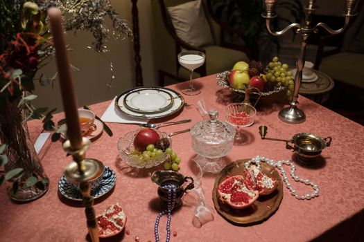 Luxurious dinner table setup with fruits, pearls, and vintage tableware.
