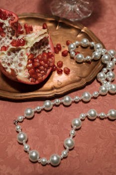 A pomegranate and pearl necklace elegantly displayed on a tray with a pink background.
