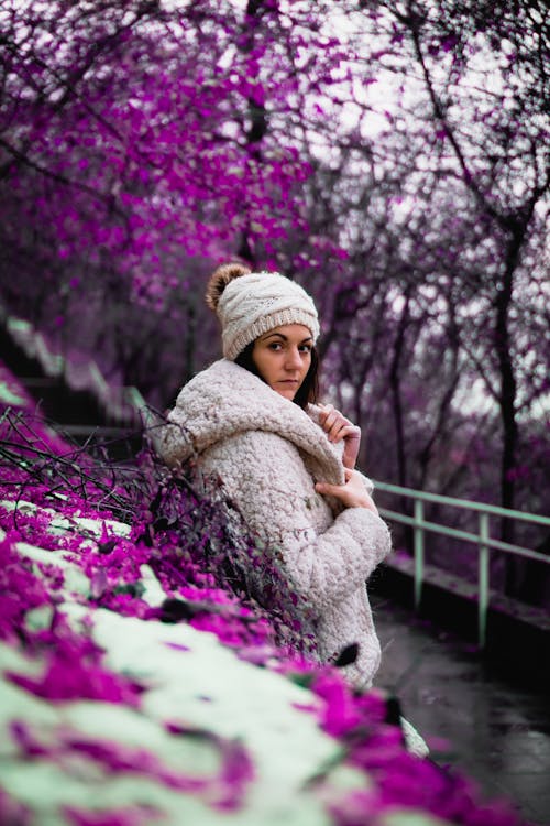 Woman in Winter Clothing Posing Beside Purple Flowers